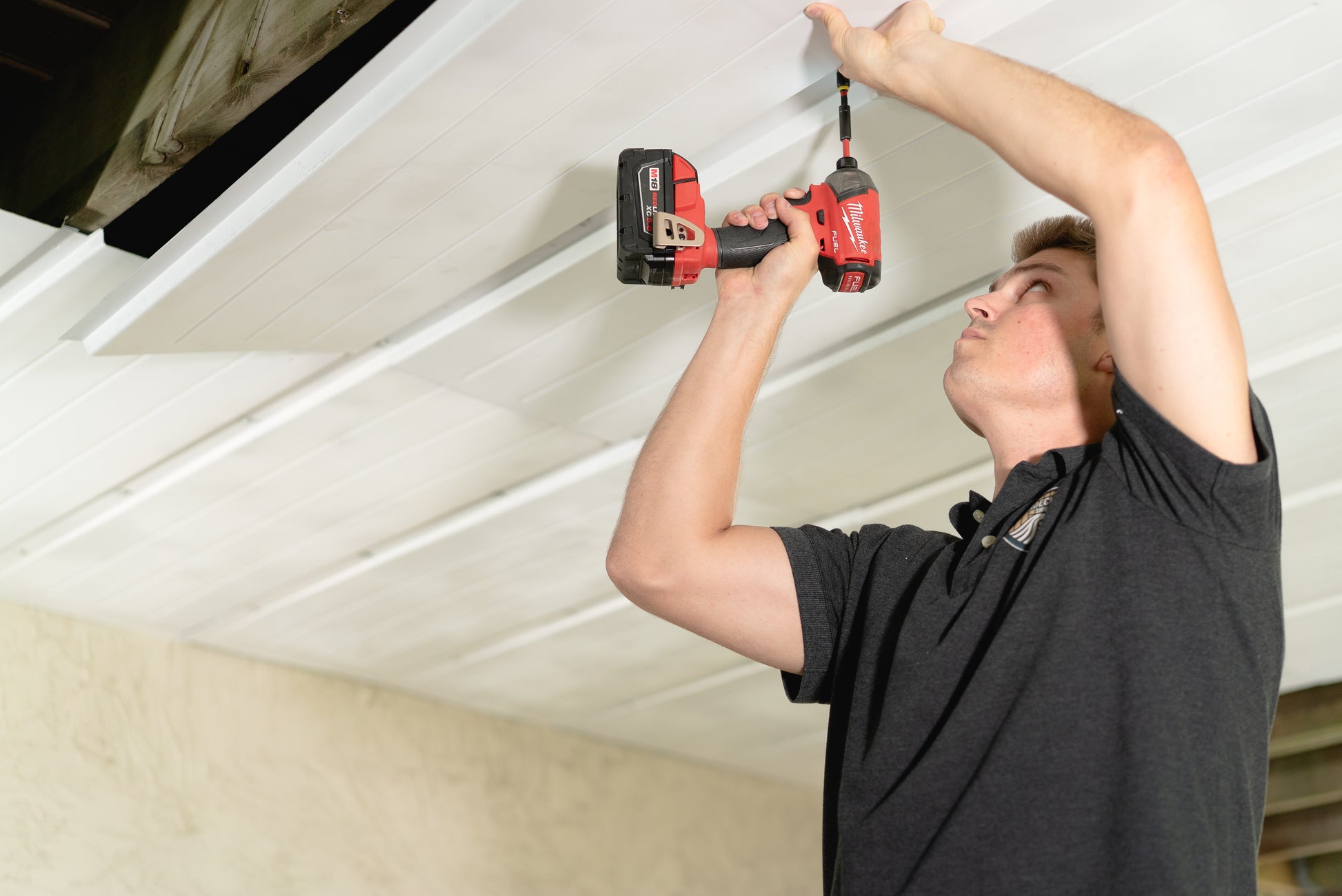 Person installing an UnderDeck Shields panel with a cordless drill.