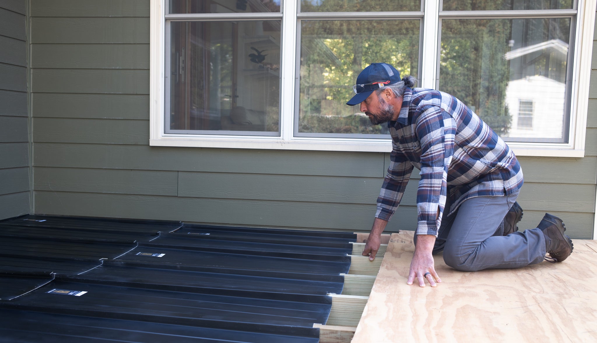 Person installing UnderDeck Shields panels on the topside of a deck attached to a house.