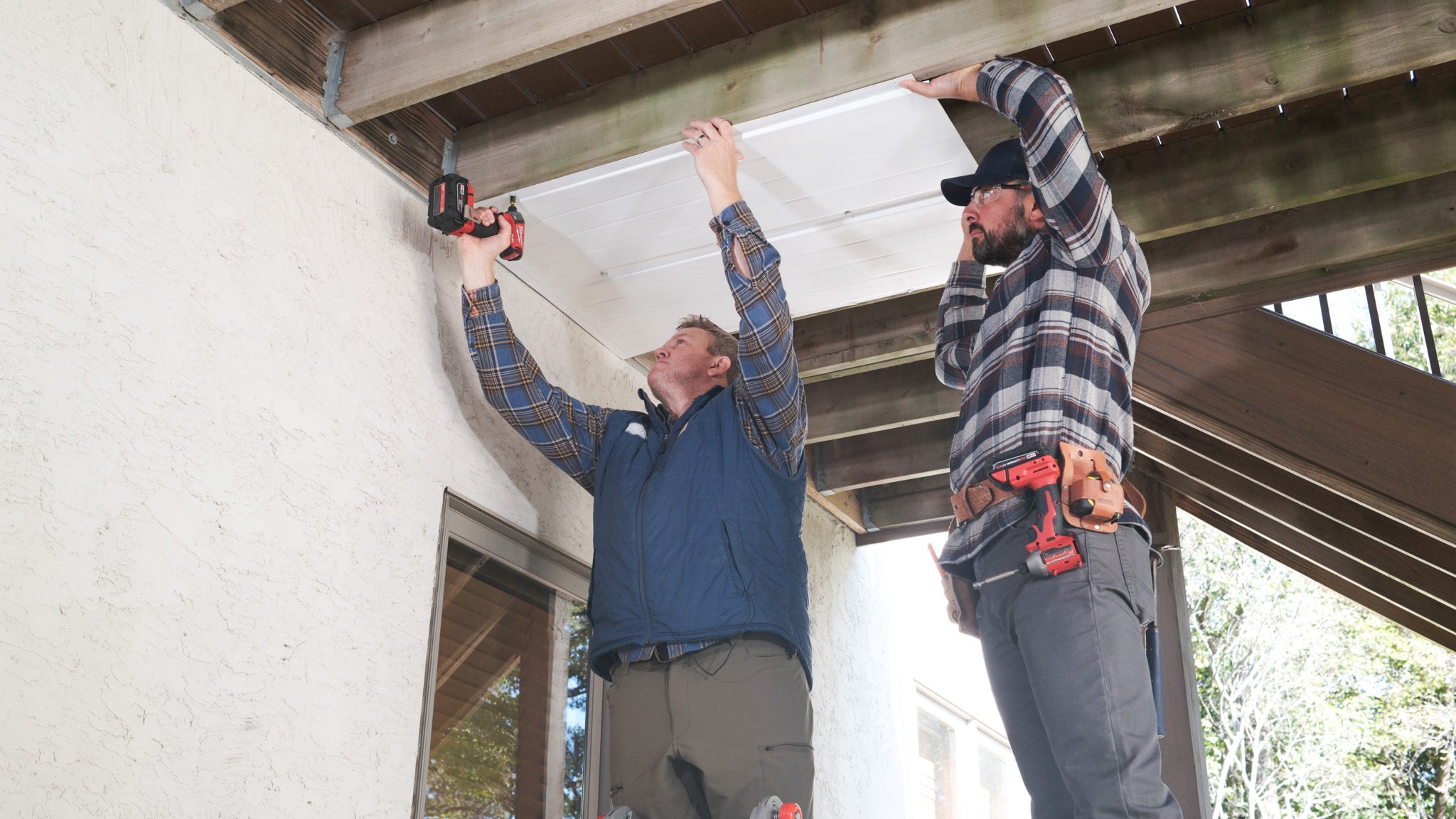 Two people installing UnderDeck Shields panels on the underside of a deck.
