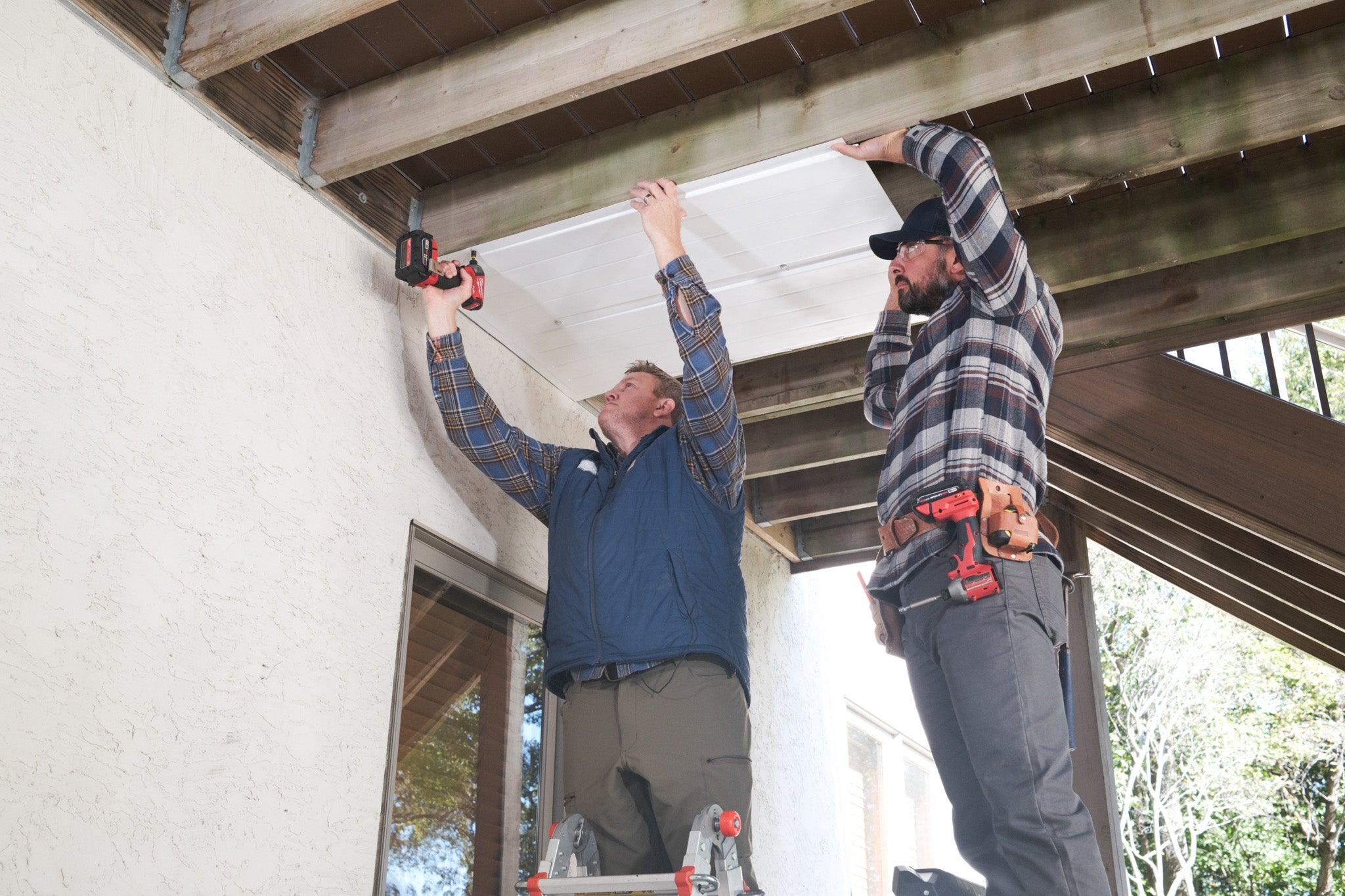 Two people installing UnderDeck Shields panels on the underside of a deck.